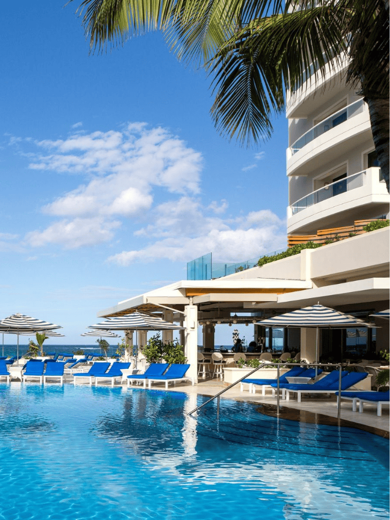Luxury oceanfront hotel with pool and tropical palm trees at sunset, perfect vacation destination.
