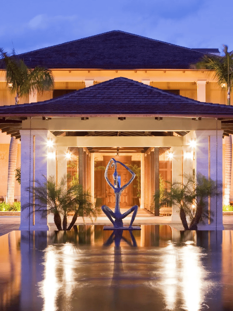 Elegant luxury resort entrance with water fountain, lush palm plants, and ambient lighting at dusk.