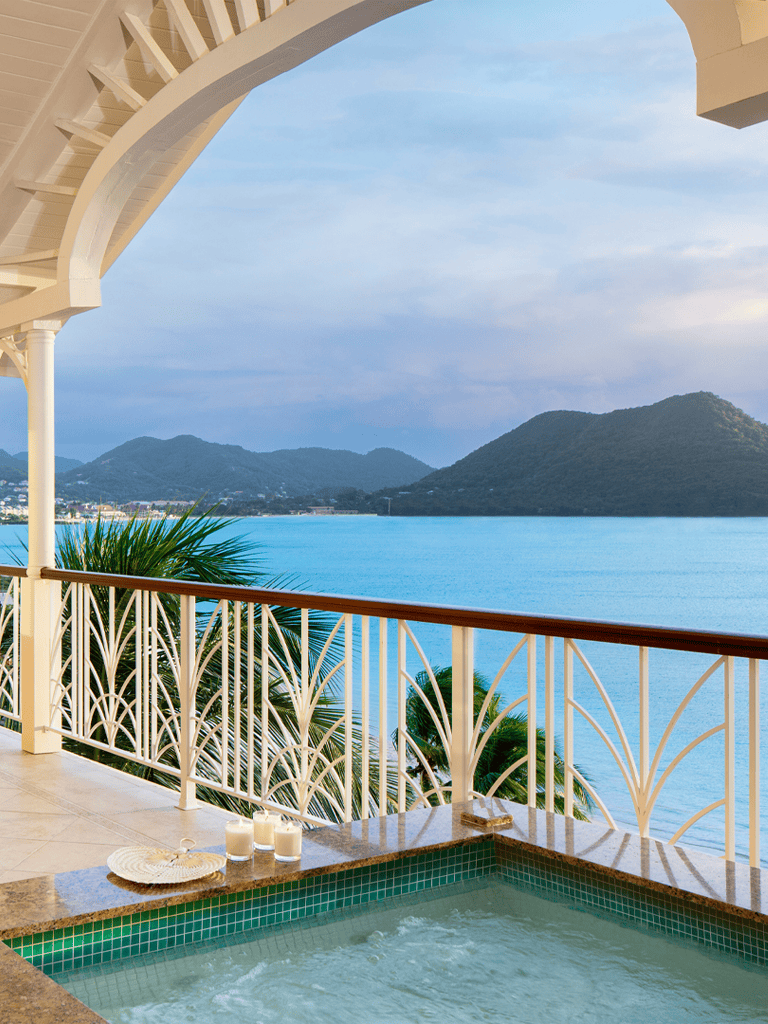 Serene ocean view from a balcony with hot tub, lush mountains, and clear blue skies, perfect for relaxation.