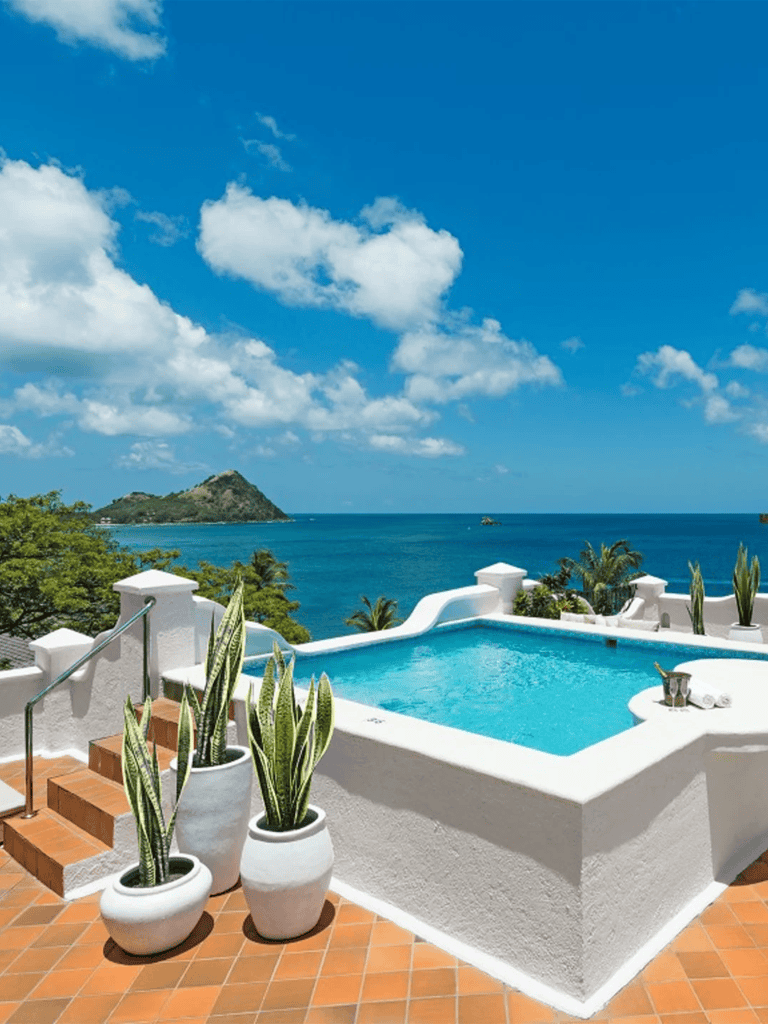Stunning oceanview pool with white exterior, tropical plants, and turquoise waters of the Caribbean.