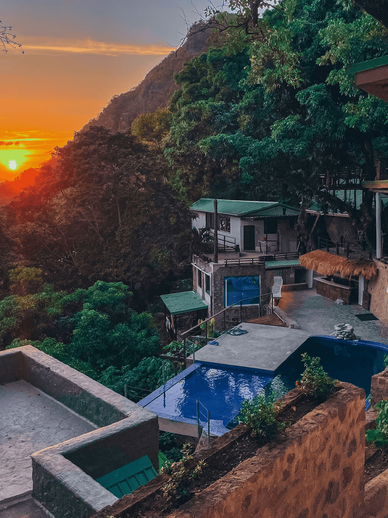 Sunset view at a tropical eco-resort with swimming pools surrounded by lush greenery and mountains.