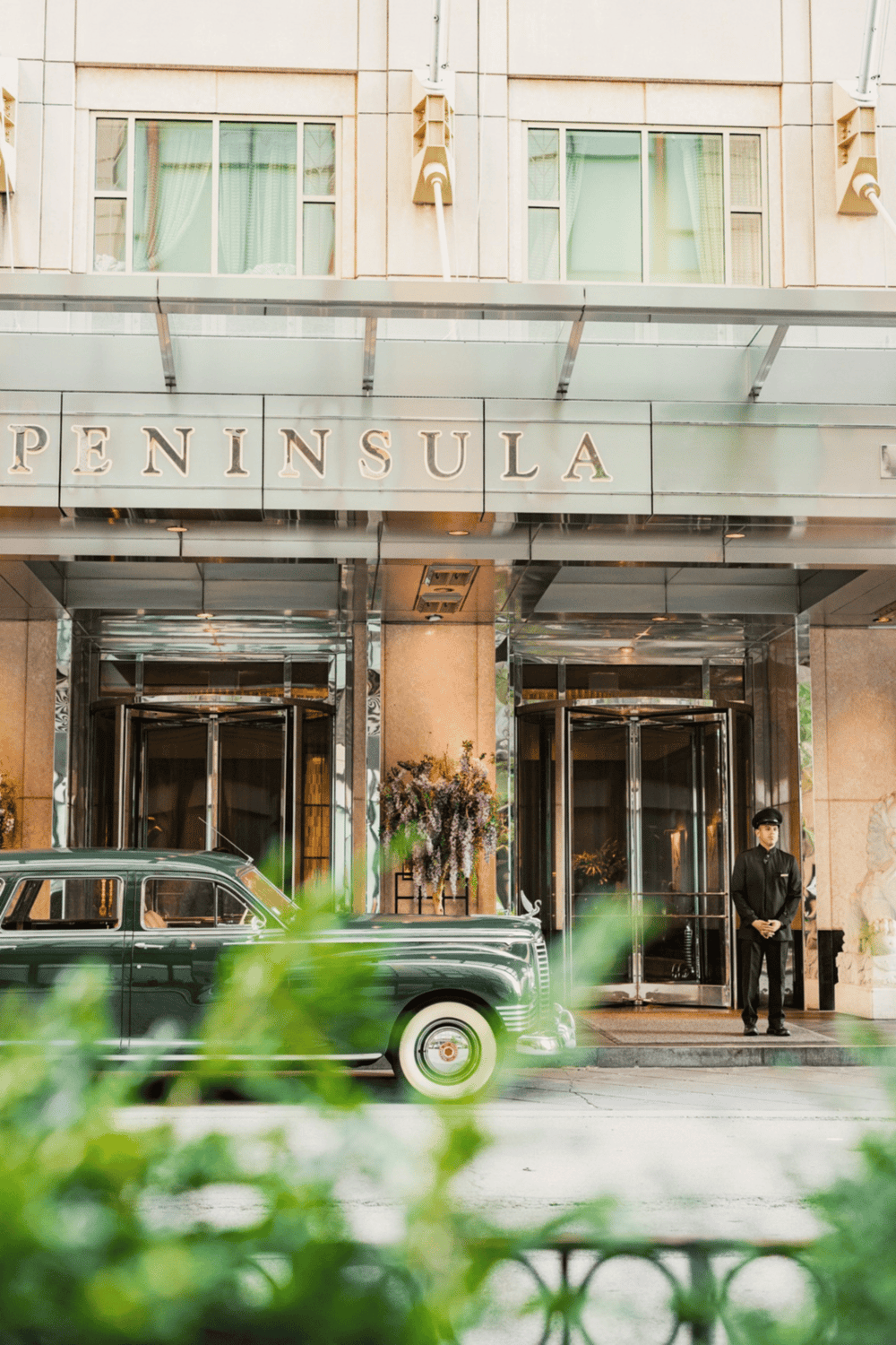 Luxury hotel entrance at The Peninsula with classic car and friendly staff, perfect for upscale travel.