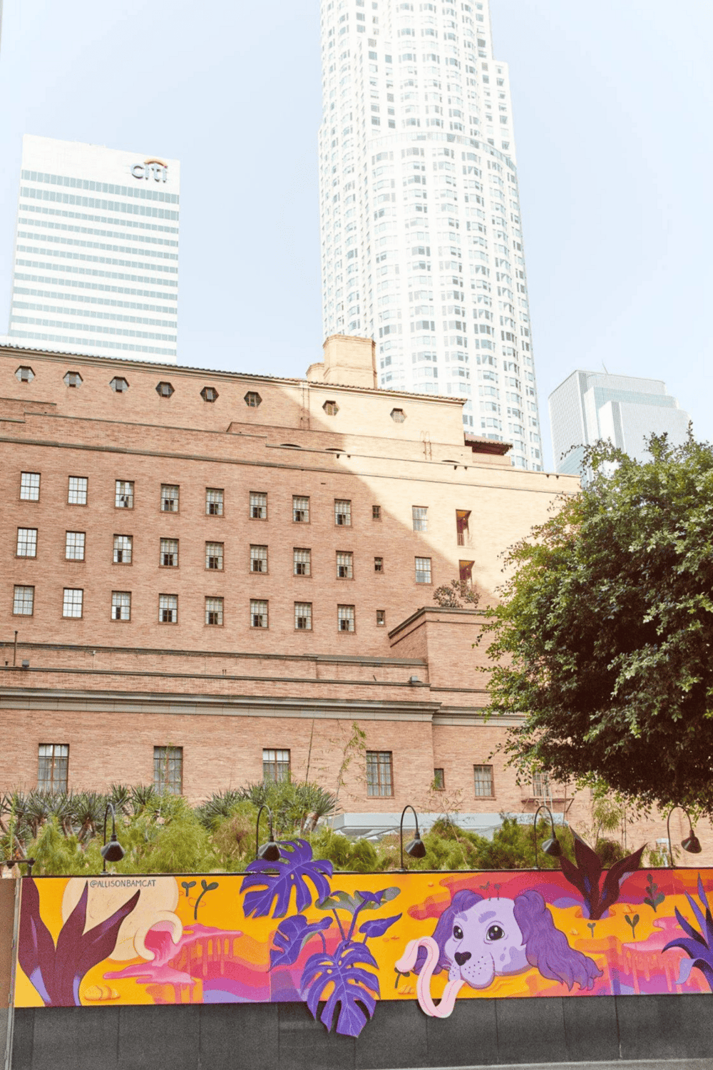 Vibrant cityscape with rainforest mural, modern skyscrapers, and historic brick building in downtown LA.