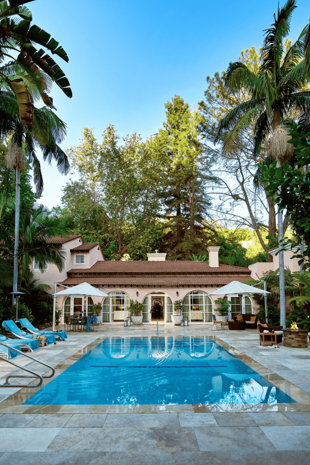 Relaxing outdoor swimming pool surrounded by lush tropical trees and luxury lounge chairs.