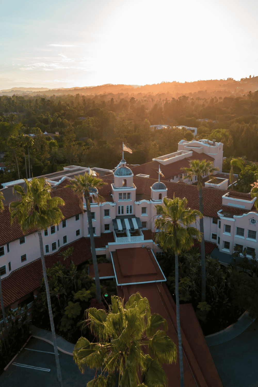 Elegant hotel surrounded by palm trees with scenic mountain views at sunset.