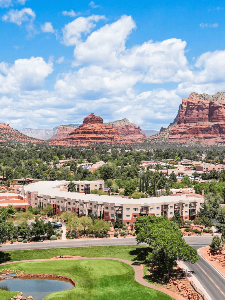 Vibrant desert landscape with red rock formations and urban residential area, sunny sky, and lush greenery.