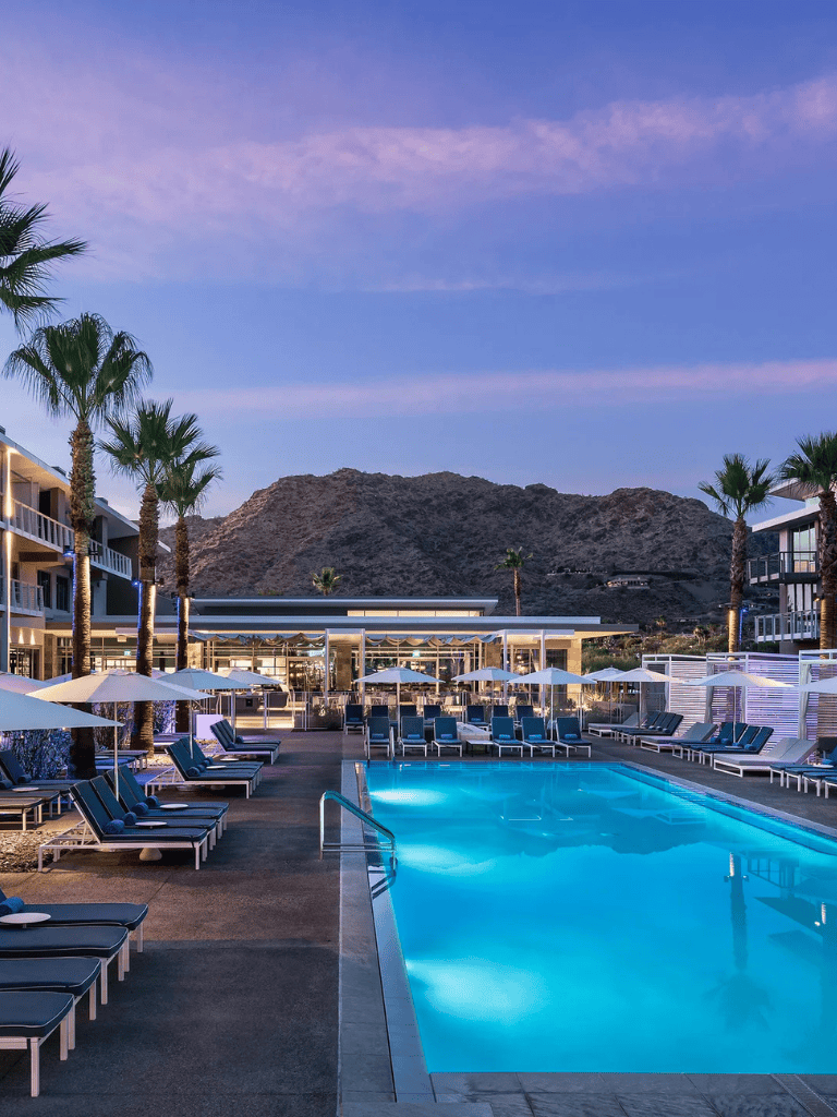 Relaxing hotel pool with mountain view at sunset, palm trees, and modern amenities.
