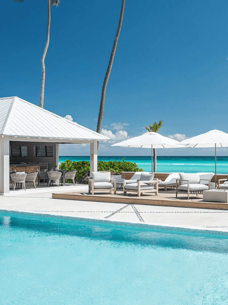 Relaxing tropical beach resort with pool, lounge chairs, and umbrellas under blue sky.