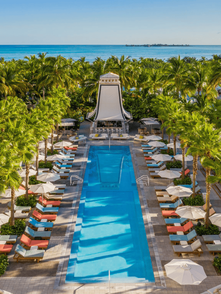 Luxurious beachfront resort swimming pool with cabanas and palm trees, ocean view in the background.
