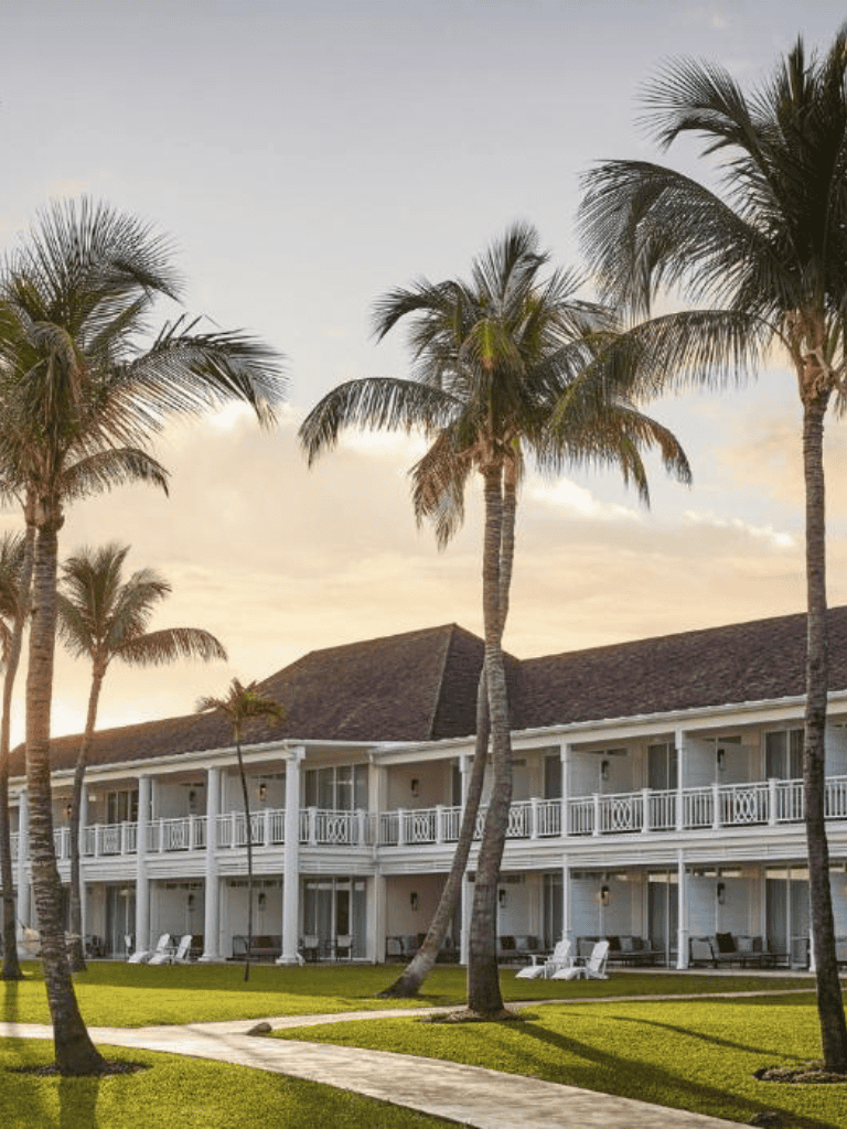 Palm tree resort accommodation with lush green lawn and sunset sky.