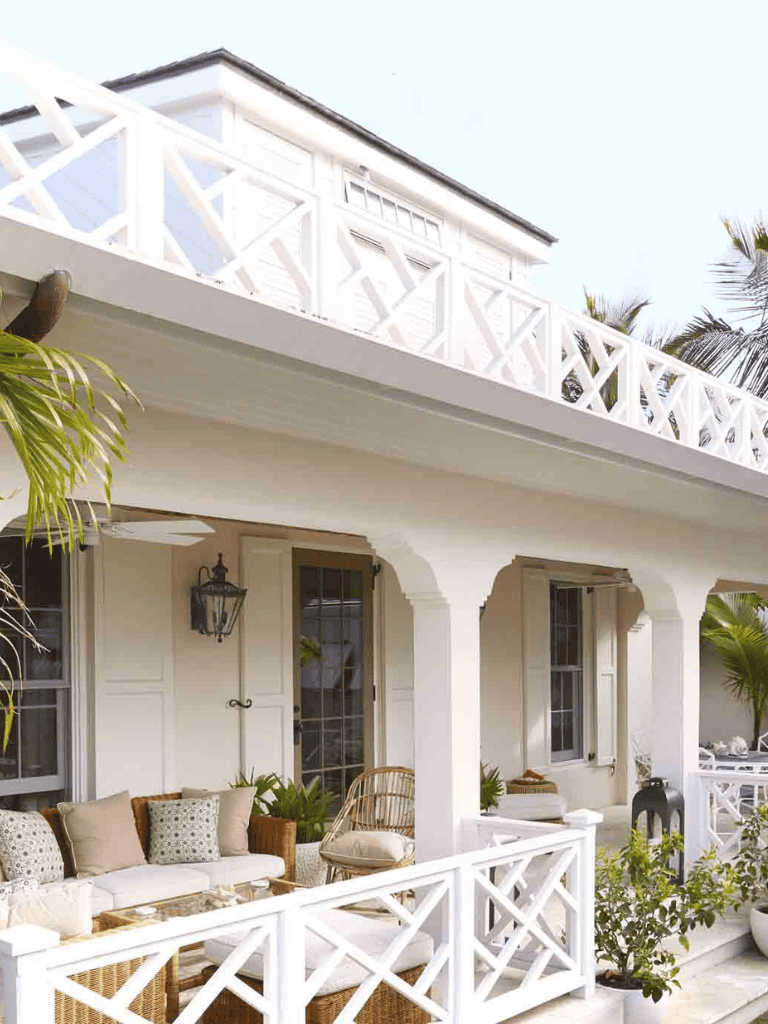 Charming white coastal house with a spacious balcony and lush greenery, perfect for beachside relaxation.