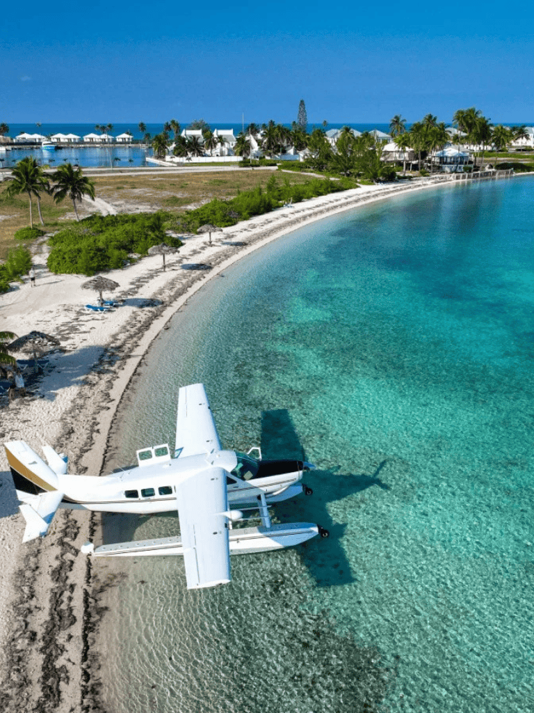 Seaplane on tropical beach with clear turquoise waters and waterfront villas in the background.