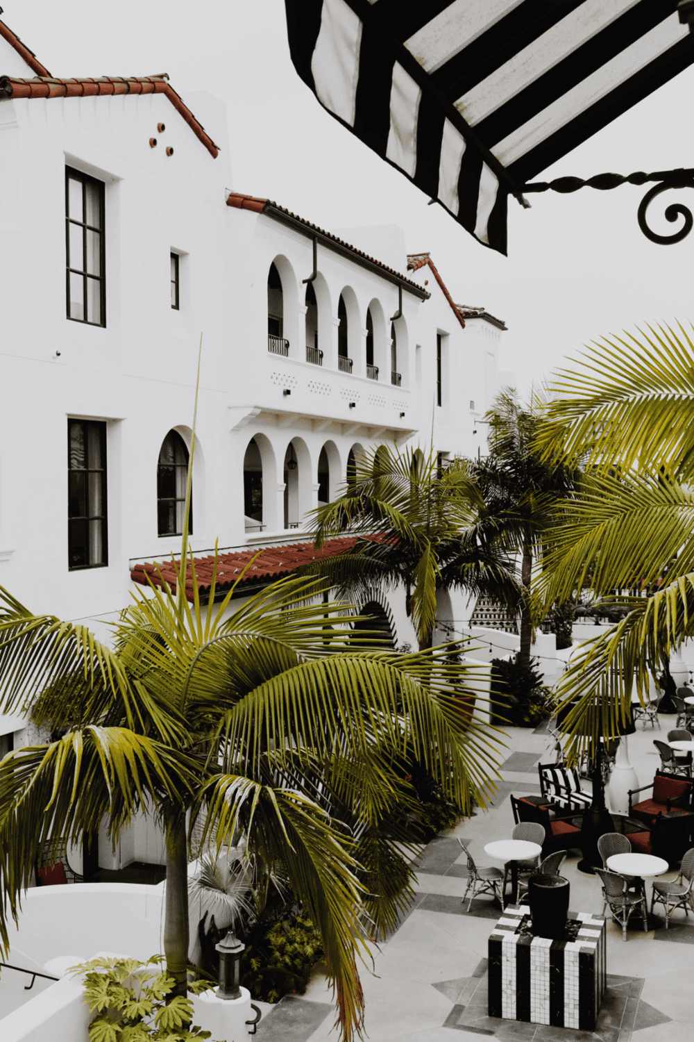 Elegant white Spanish-style building with a courtyard, lush palm trees, and outdoor seating.