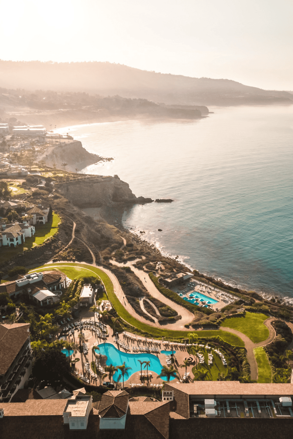Panoramic view of a coastal resort with swimming pools and ocean, scenic hillside landscape, luxury vacation destination, QuestForDirections.