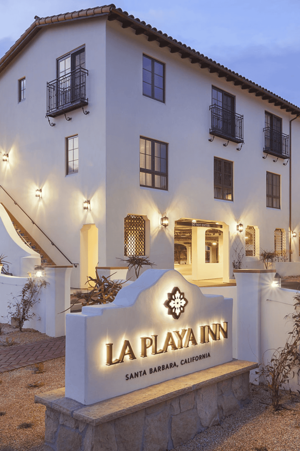 Elegant Santa Barbara hotel exterior in evening light with La Playa Inn sign, Mediterranean architecture, and cozy ambiance.