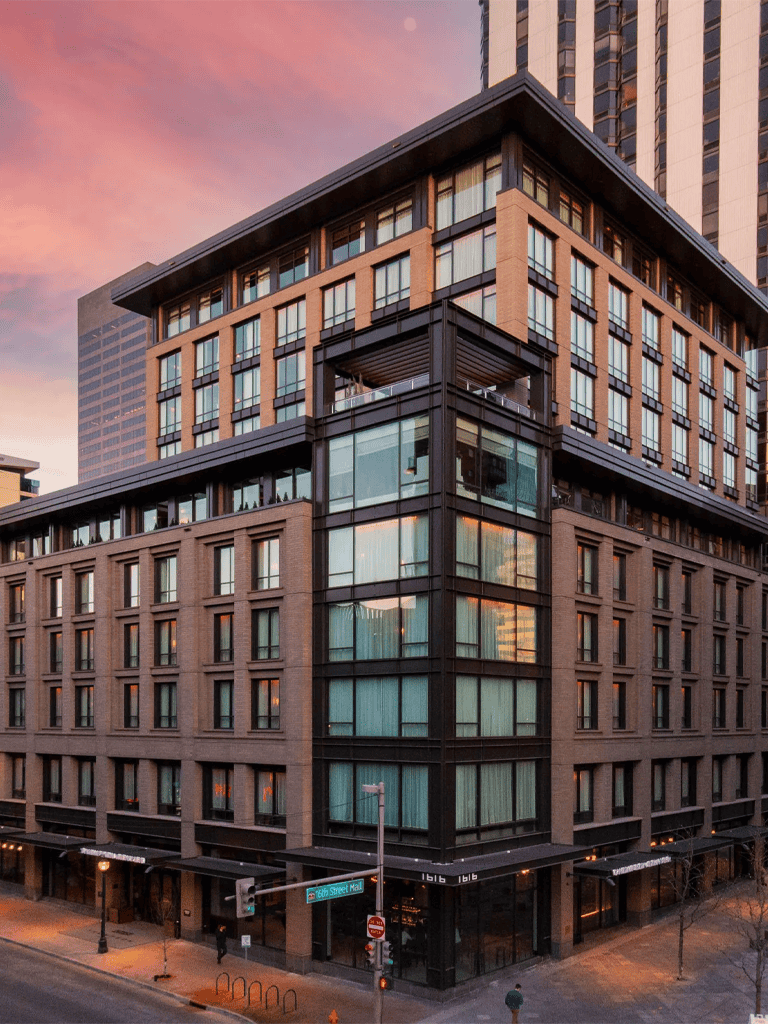 Modern urban hotel building with glass windows and city street view at sunset.
