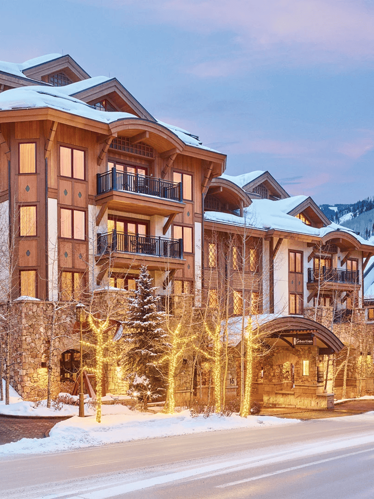 Charming mountain lodge with illuminated trees, snow-covered roof, and cozy ambiance in winter.