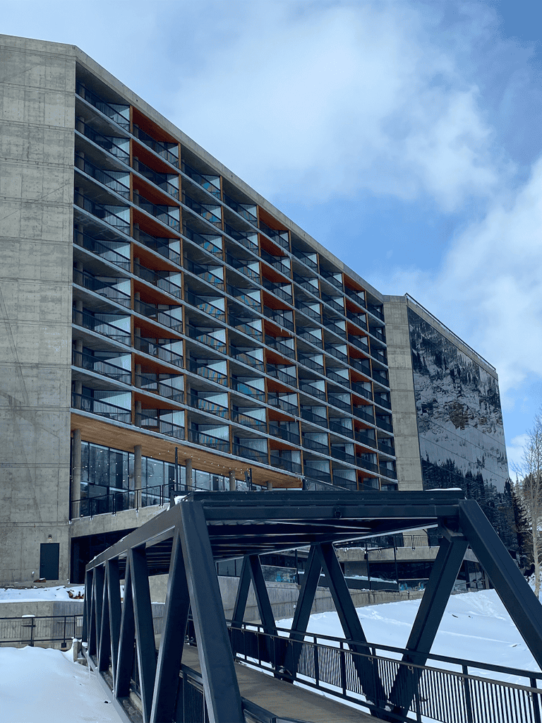 Modern hotel building with multiple balconies and a bridge in snowy landscape, scenic mountain view.