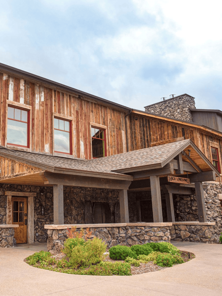 Rustic mountain lodge with stone and wood exterior, scenic landscape, outdoor entrance, and cozy mountain retreat vibe.