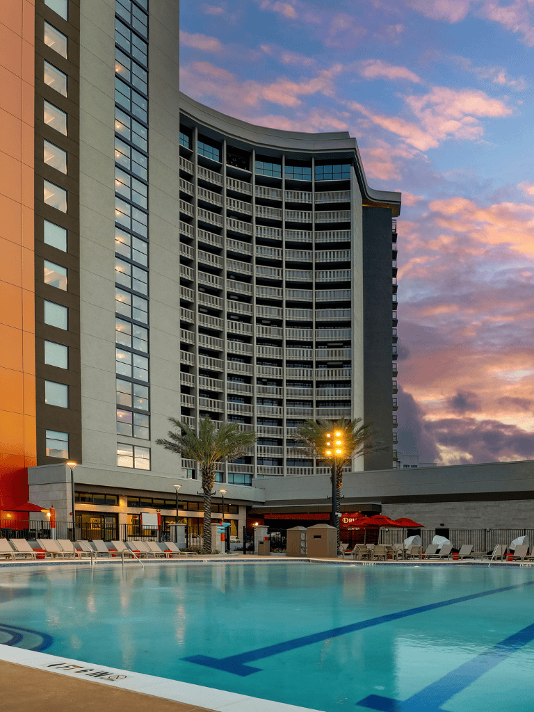 Luxury hotel high-rise with pool at sunset, modern building with palm trees, perfect for travel and leisure.