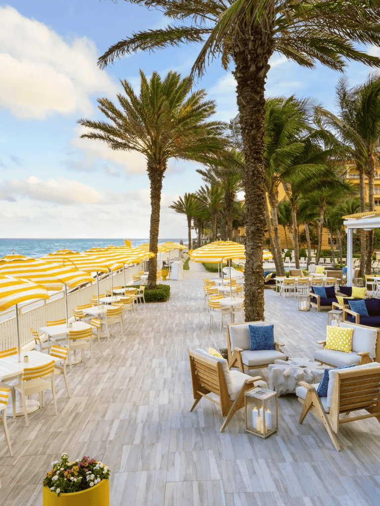 Relaxing beachfront outdoor lounge with palm trees and yellow striped umbrellas.