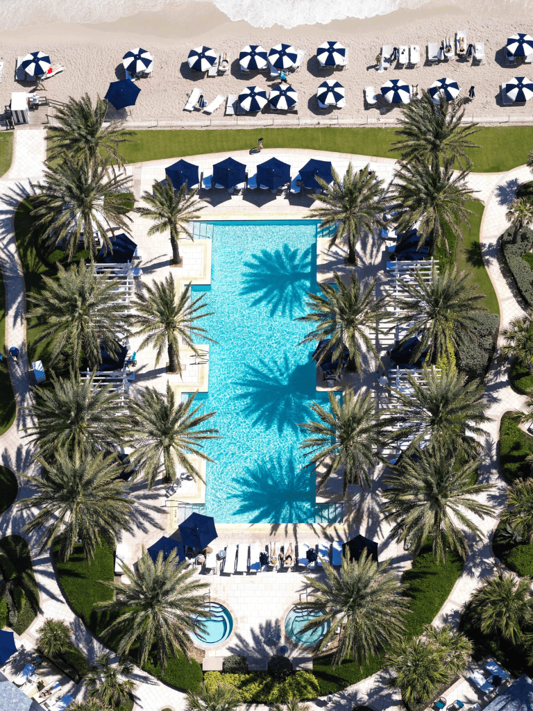 Luxurious resort pool with palm trees and shaded lounging areas, perfect for relaxation and vacation.