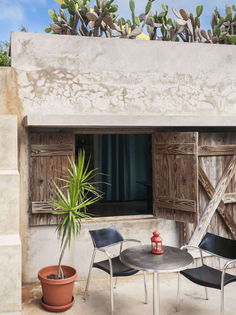 Sunlit outdoor seating area with rustic wooden window shutters and potted plant at QuestForDirections.