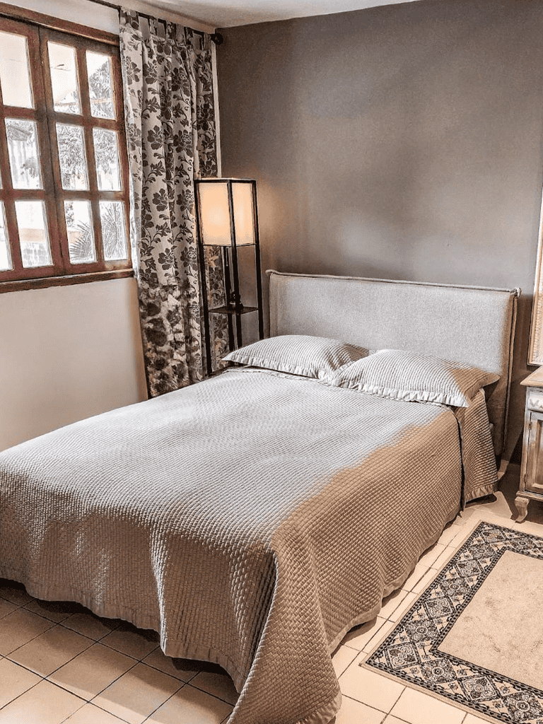 Cozy bedroom with neutral decor, contemporary lamp, floral curtains, and large window for natural light.