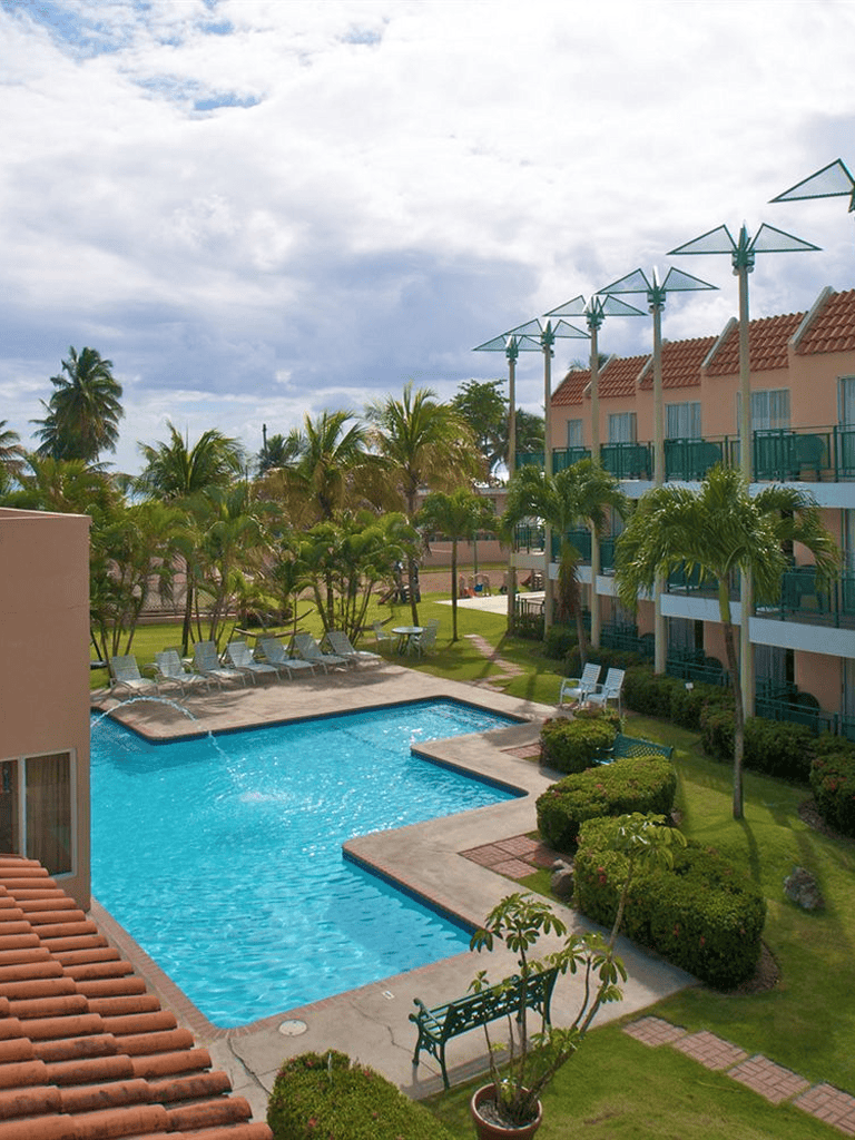 Relaxing poolside view at a tropical hotel resort with palm trees and outdoor lounge chairs.