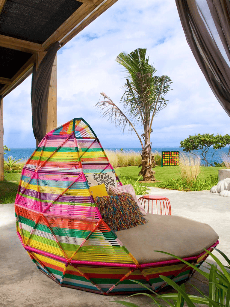 Colorful outdoor lounge chair overlooking tropical beach scenery with palm trees.