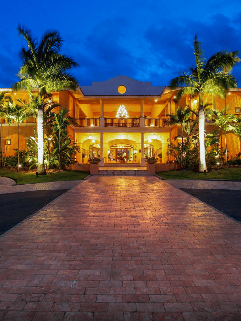 Luxurious tropical mansion with palm trees and elegant architecture at sunset.