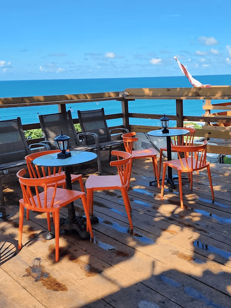 Seaside outdoor dining area with ocean view and wooden deck, perfect for relaxing meals.