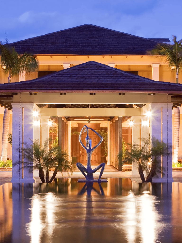 Elegant resort entrance with sculpture and pool at dusk.