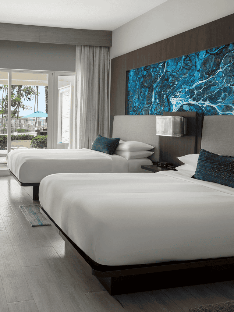 Modern hotel room with two queen beds, ocean-view balcony, stylish decor, and comfortable amenities for guests.