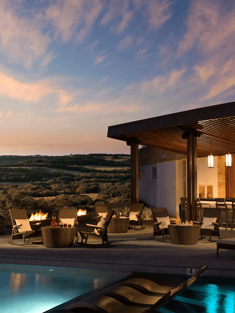 Outdoor luxury poolside lounge area with fire pits and scenic landscape views at sunset.