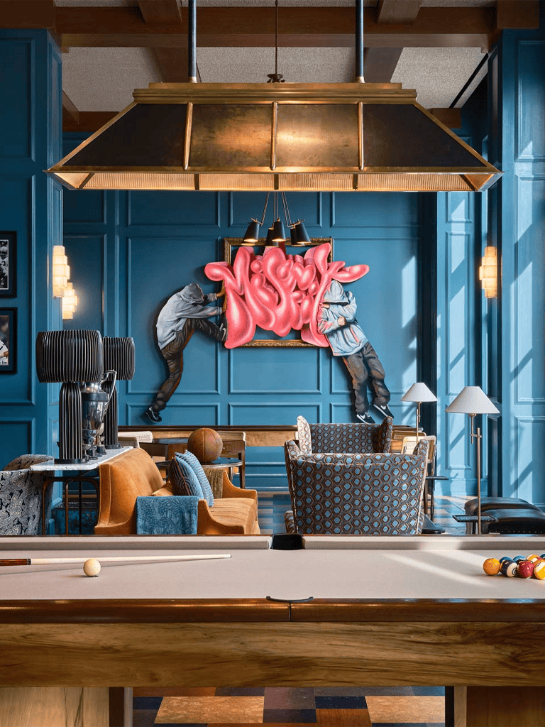 Vibrant game room with pool table, modern blue wall, graffiti art, and cozy seating area.