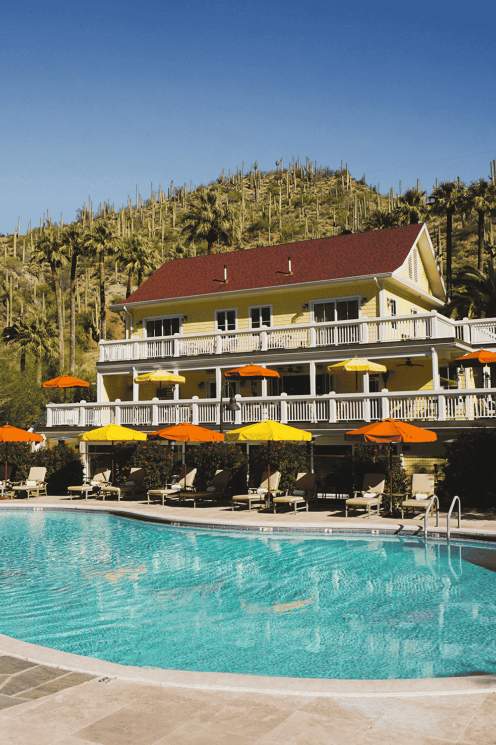 Luxury resort swimming pool with yellow and orange umbrellas, scenic mountain background, perfect for vacation relaxation.
