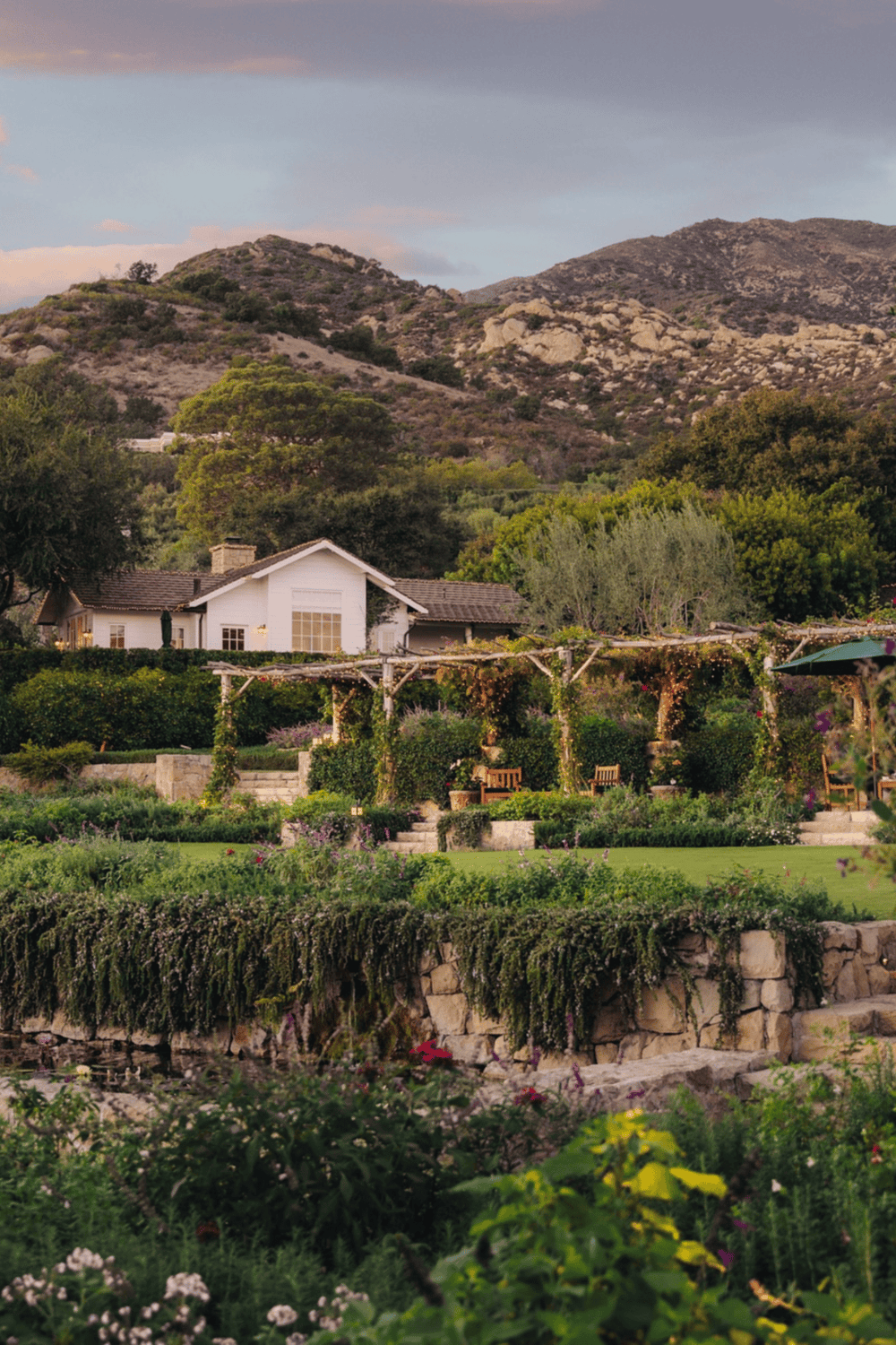Serene garden with mountains, house, and outdoor seating, featuring lush greenery and scenic views.