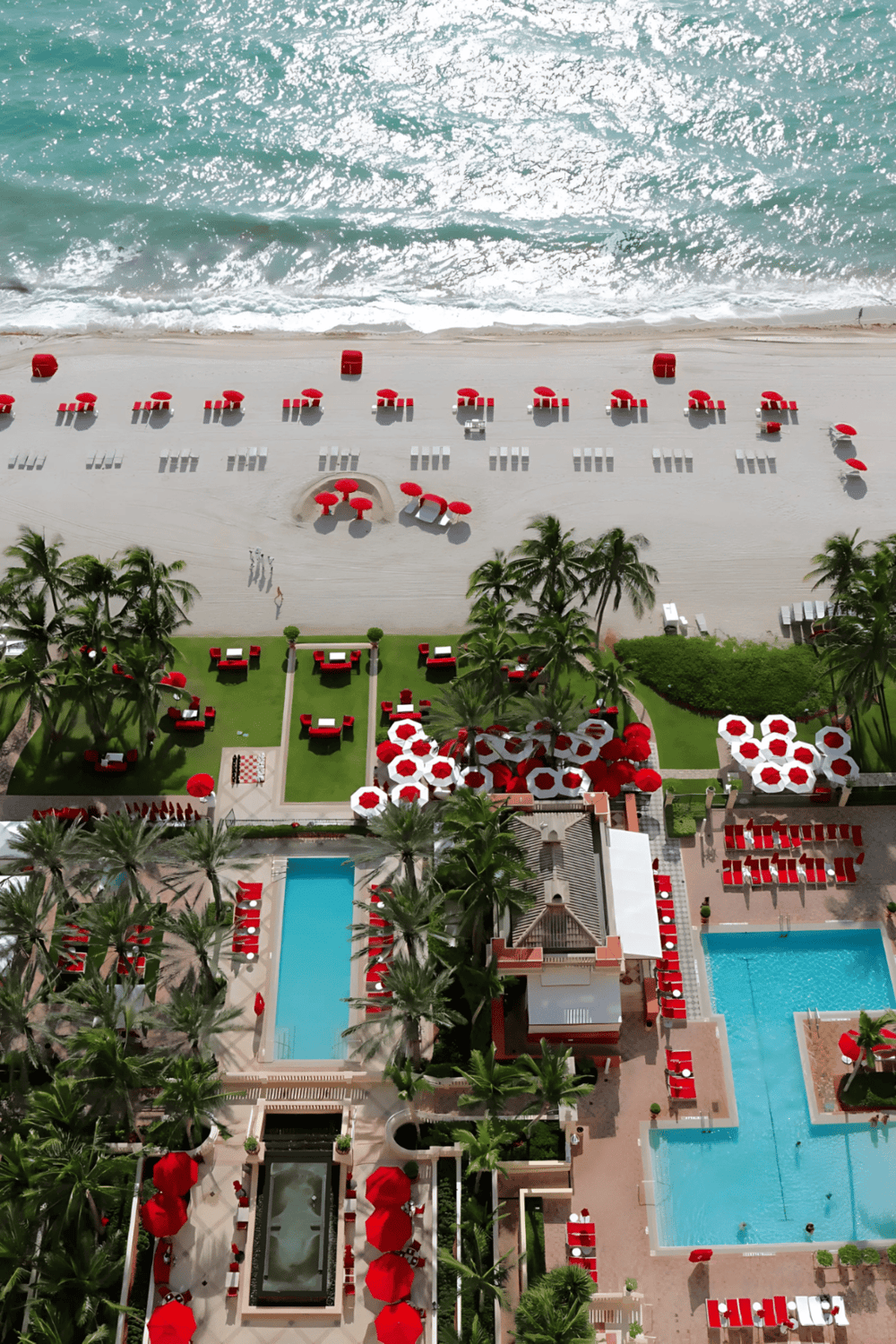 Beach resort with red umbrellas, swimming pools, and lush palm trees, perfect for luxury vacation rentals and seaside getaways.