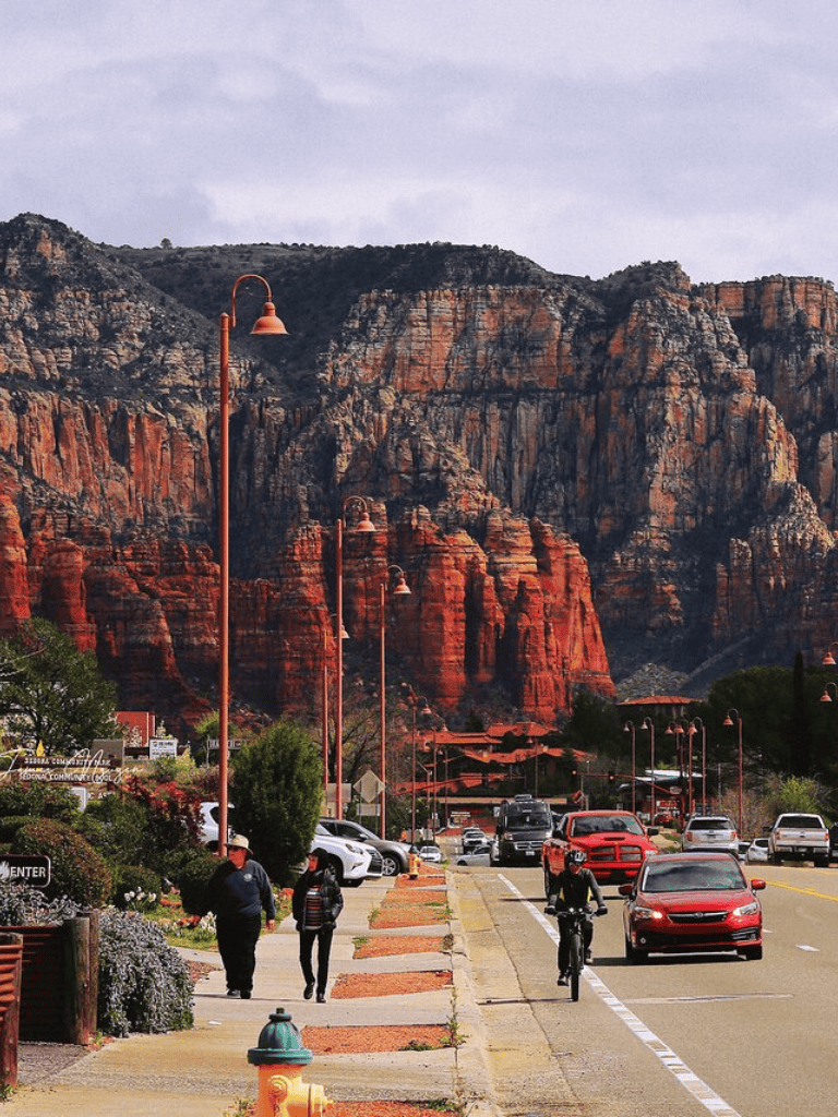 Vibrant red rock mountain scenery with walking pedestrians and parked cars in a charming town setting.