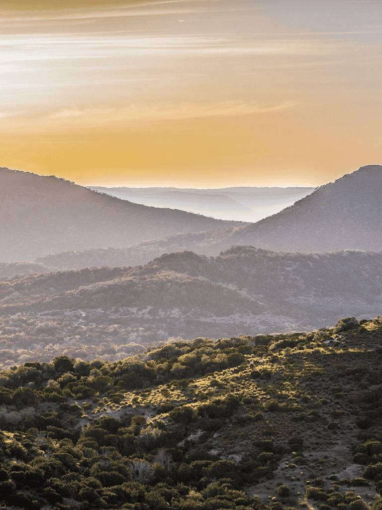 Majestic mountain landscape during sunset with layered hills and lush greenery.