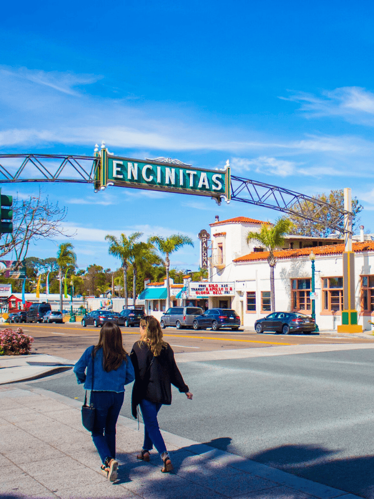 Encinitas city sign in downtown Encinitas, California, with people walking and vibrant local shops.