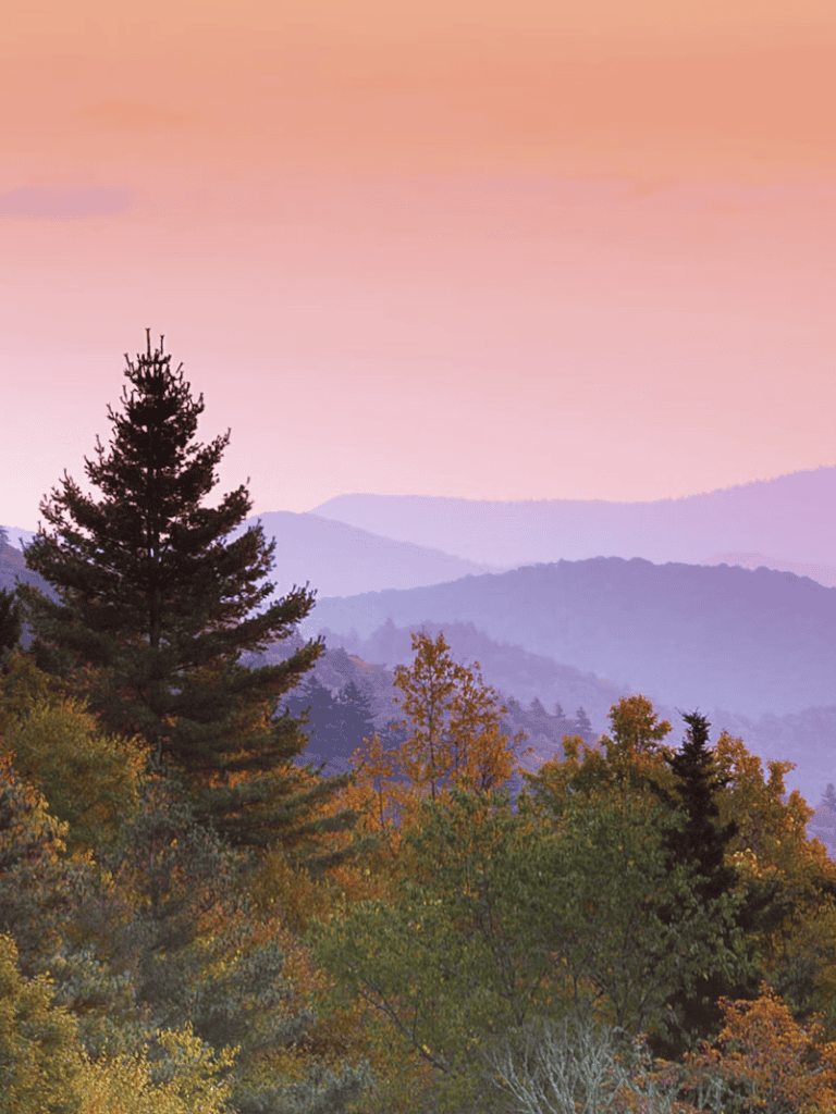 Vast mountain landscape with colorful autumn foliage and a pink sunset sky.