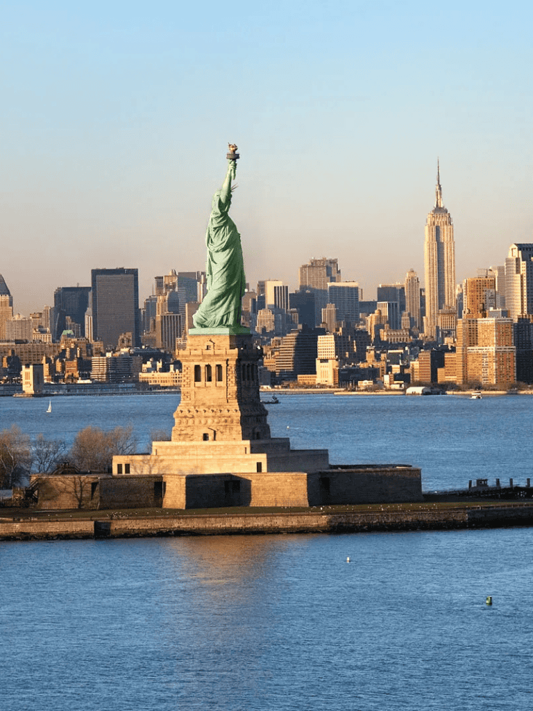 Statue of Liberty and New York City skyline at sunset, iconic American landmarks.