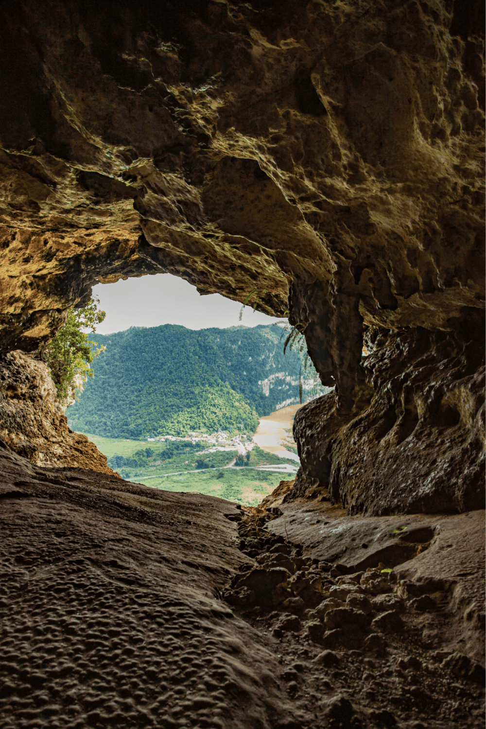 Vibrant scenic view of lush green mountains and river seen from inside a cave, showcasing nature exploration.