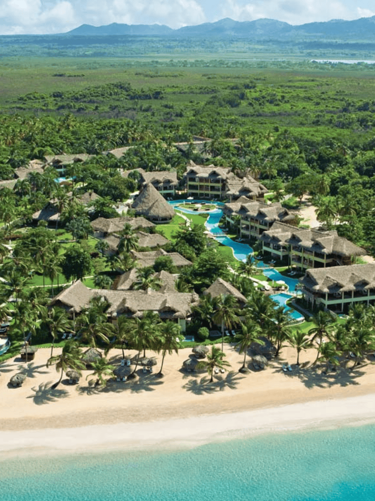 Luxurious beach resort with straw-roofed bungalows, lush greenery, and oceanfront views.