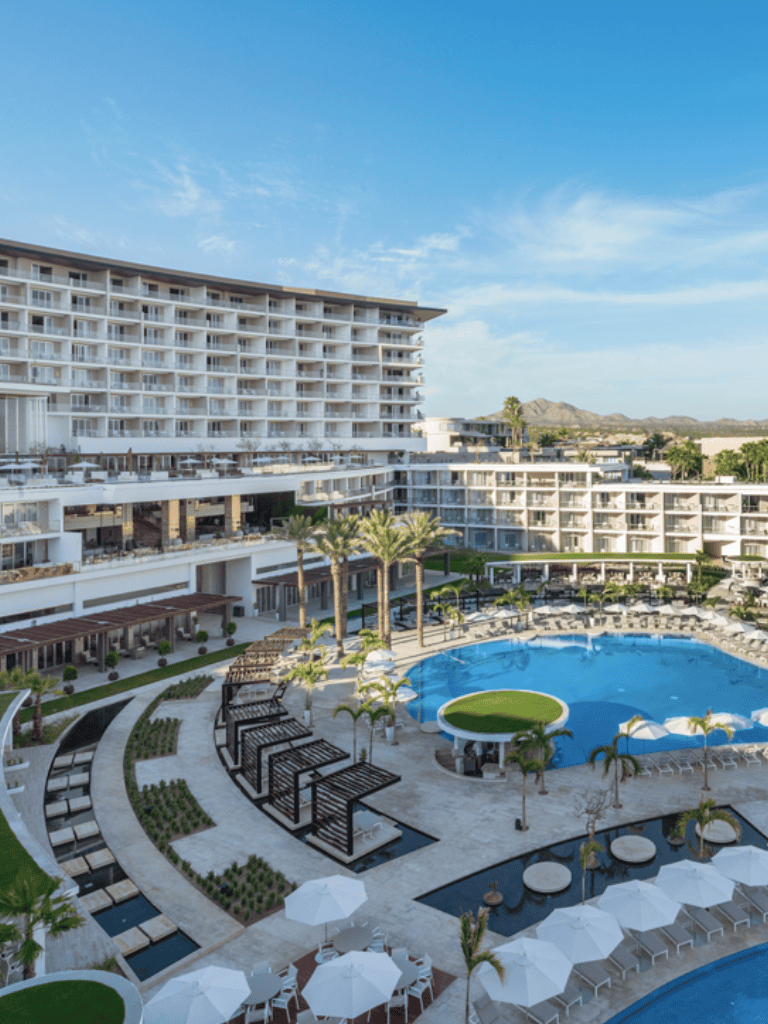 Luxury resort pool and modern hotel with sunset views, palm trees, and mountain backdrop.