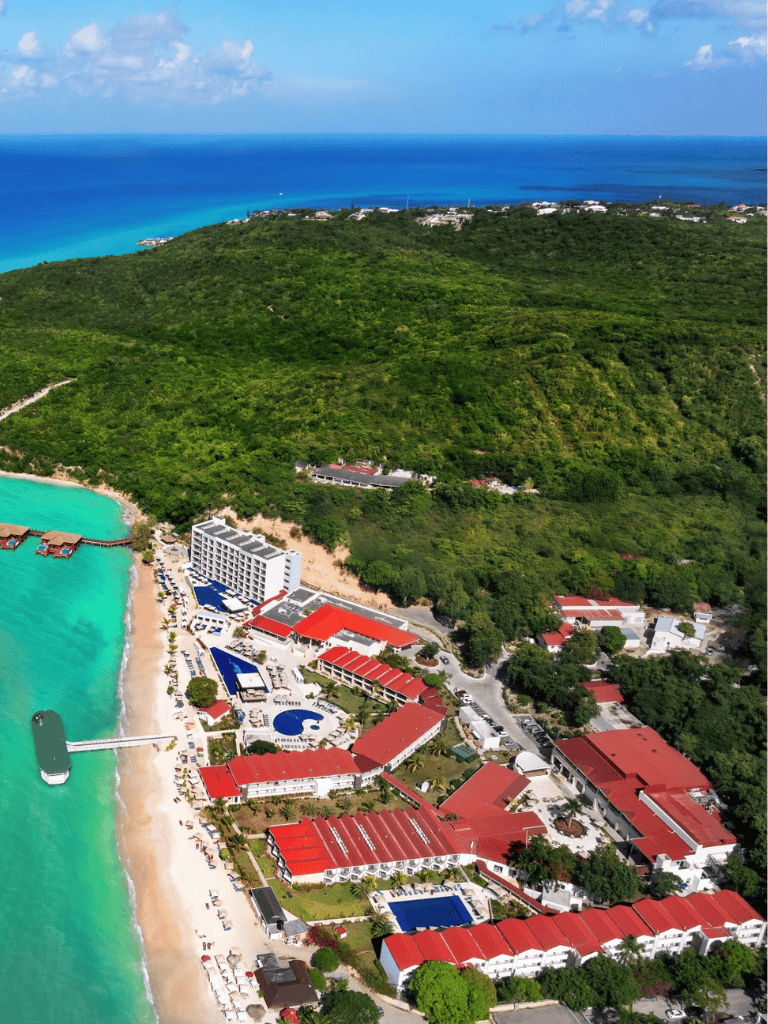 Overwater bungalows and turquoise ocean at a tropical resort with lush green hills in background.