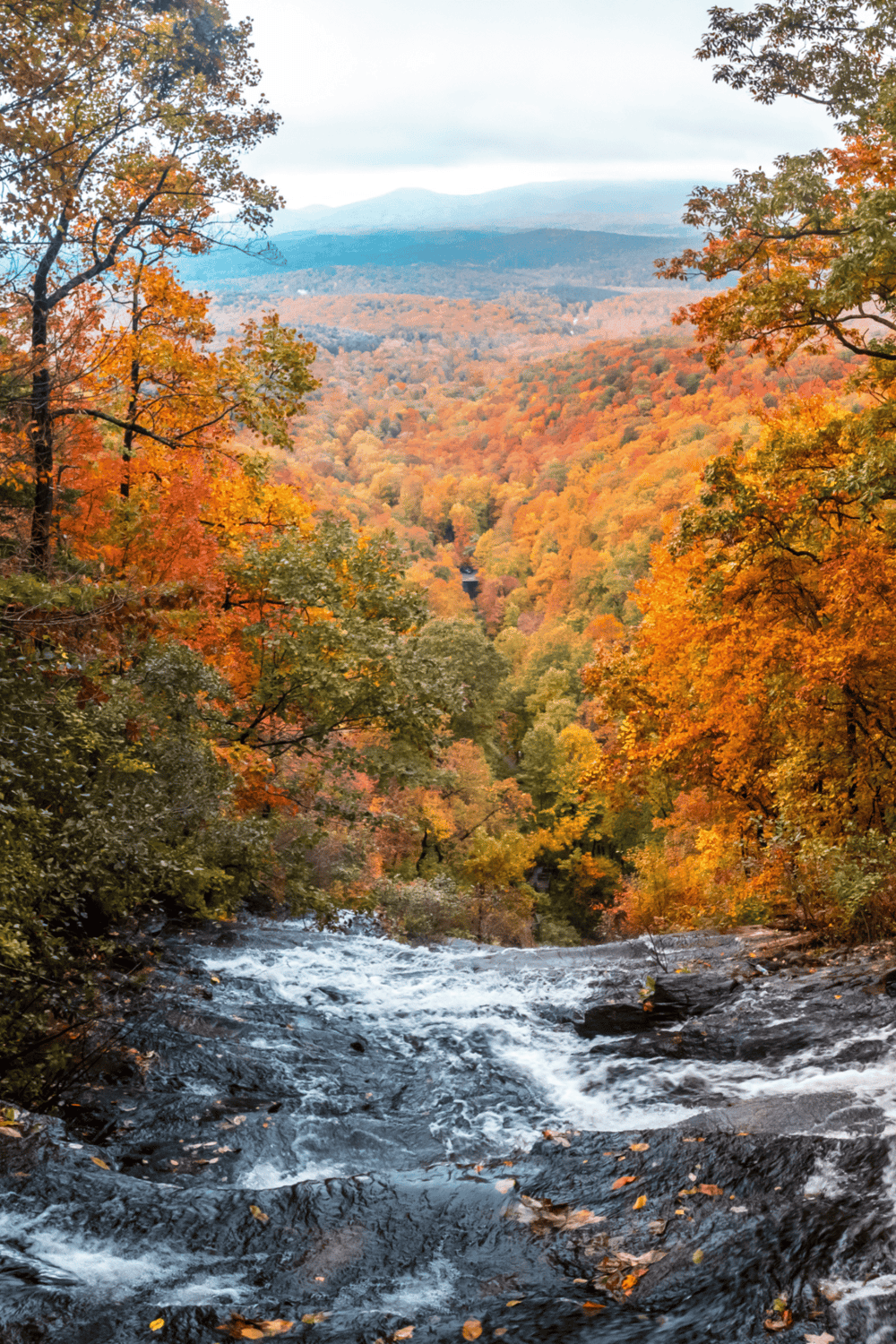 Vivid autumn landscape with water creek, colorful fall foliage, and mountainous horizon, scenic outdoor nature scene.