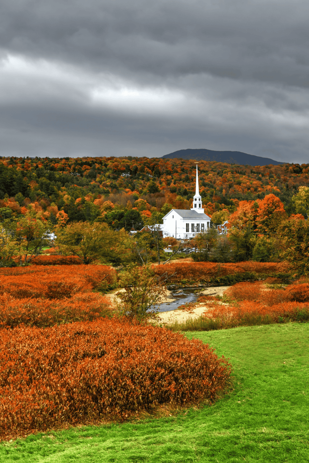 Colorful autumn landscape with church and mountain view in Vermont, scenic fall foliage and vibrant trees.